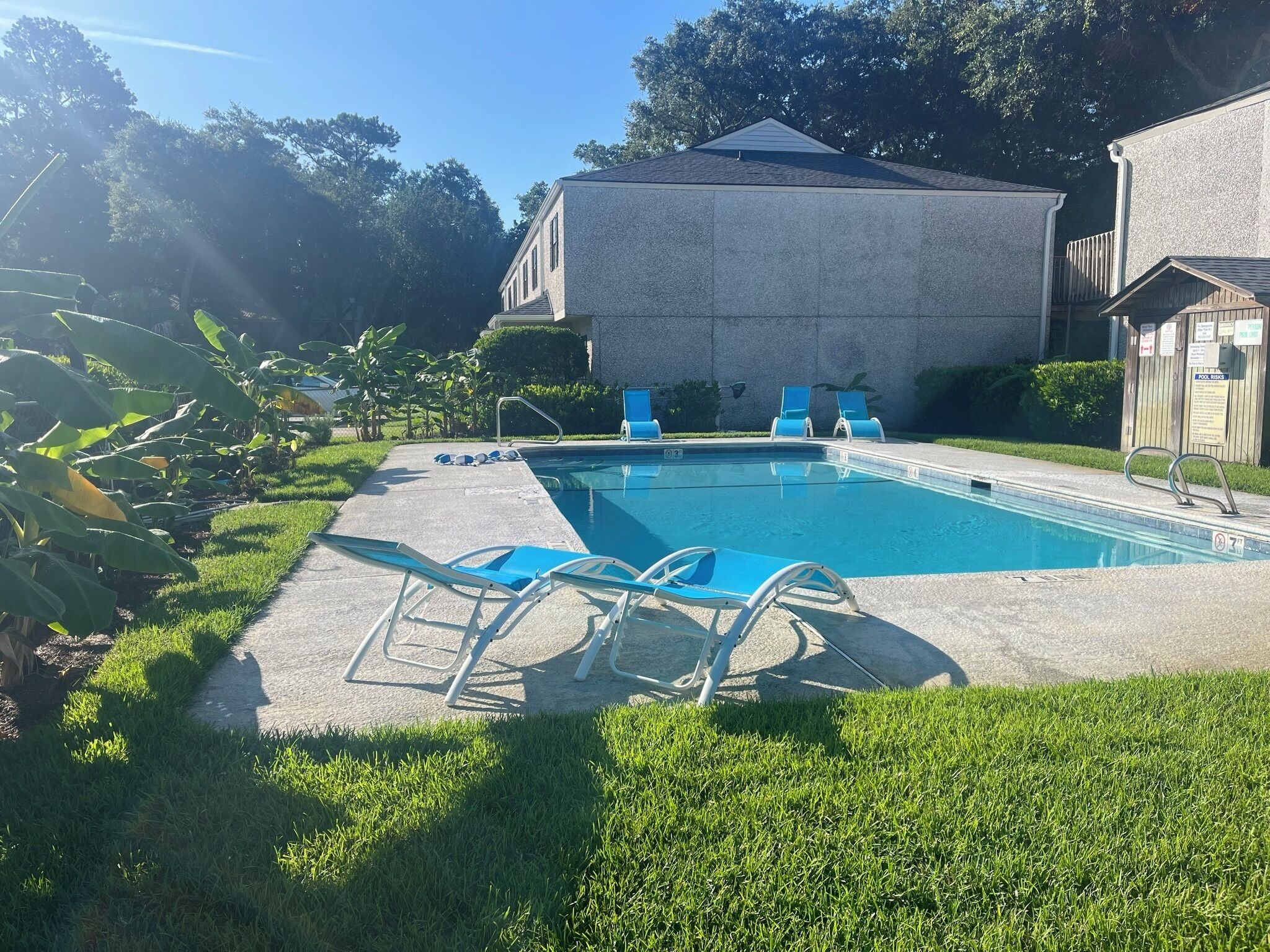 Una piscina con sillas azules, un deck de concreto y un edificio al fondo.