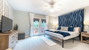 Une chambre à coucher comprenant un lit, un téléviseur, un ventilateur de plafond, une table de chevet et une fenêtre avec des rideaux.