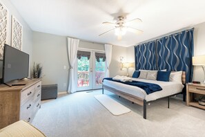 A bedroom with a bed, a TV, a ceiling fan, a nightstand, and a window with curtains. - Bring pets! Steps2pool, bike2beach, easy on/off island, 3 beds, bikes incl! (St. Simons Island)