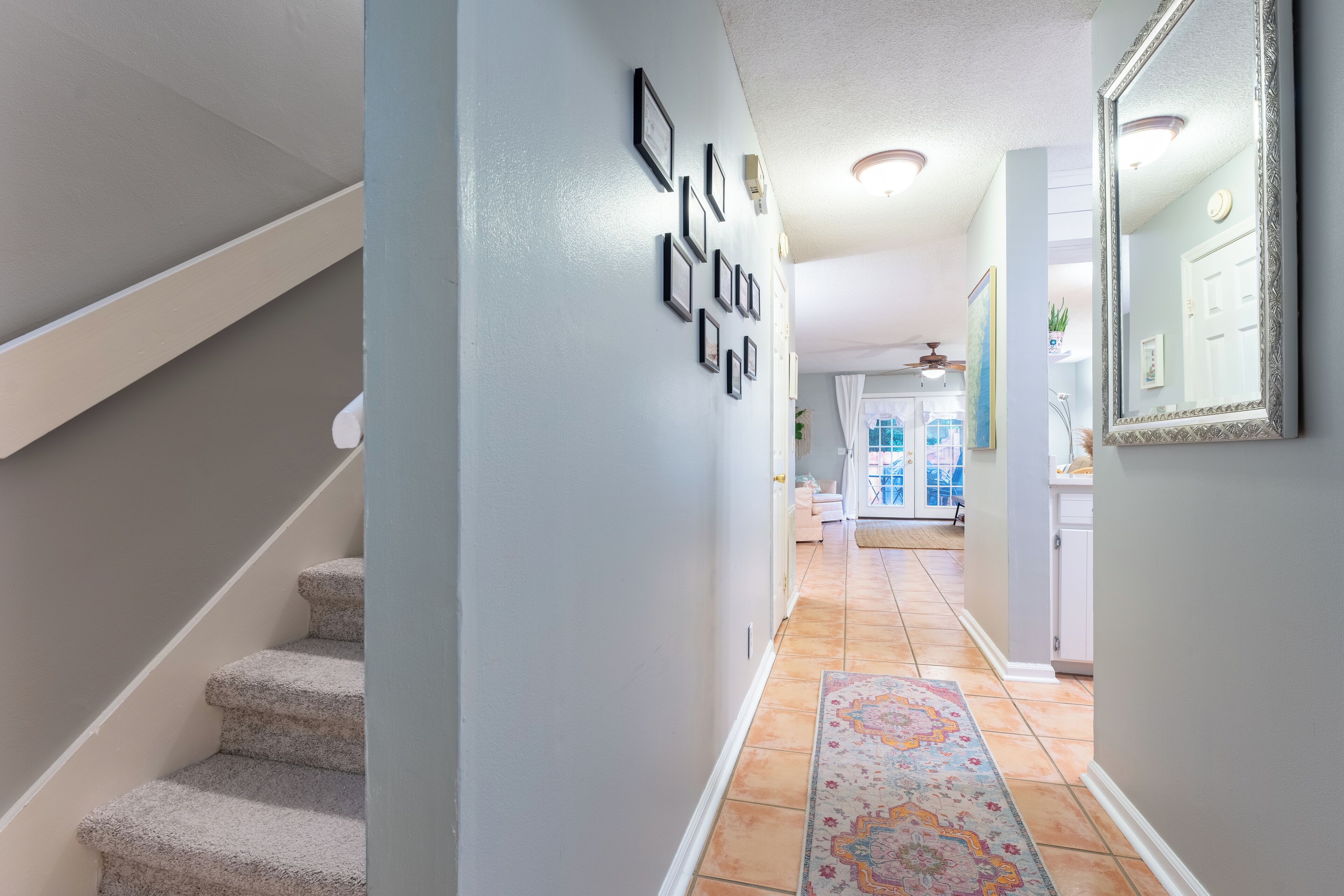 A hallway with a staircase, a patterned rug, and framed pictures on the wall.