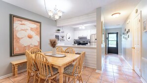 Un coin repas avec une table et des chaises en bois, un lustre et un grand tableau floral accroché au mur.