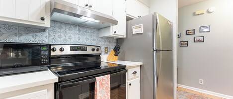 Una cocina con armarios blancos, un refrigerador de acero inoxidable, un microondas, un horno y un salpicadero de azulejos.
