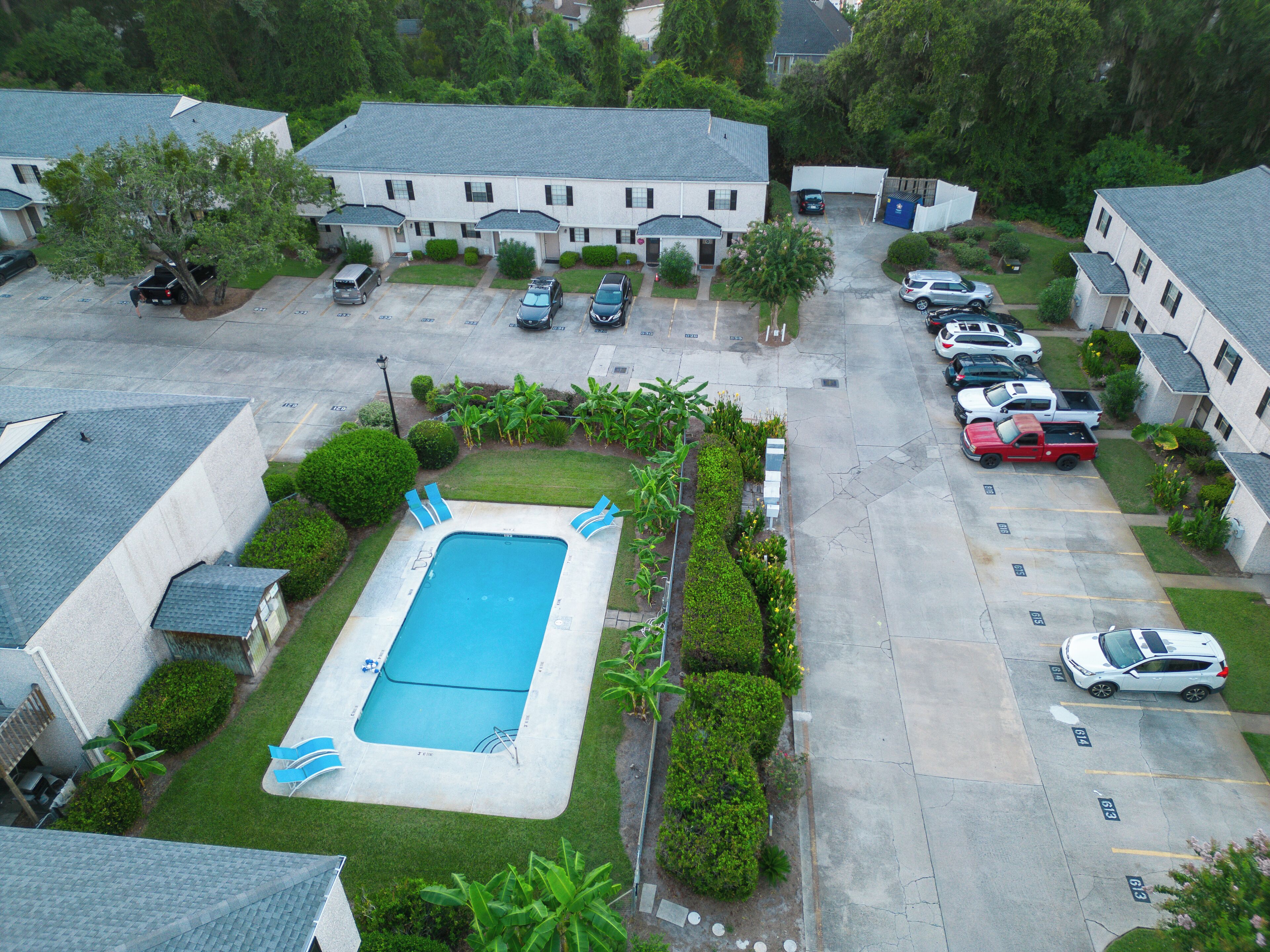 A residential area with a swimming pool, multiple parked cars, and houses with similar architecture.