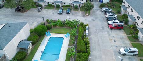 A residential area with a swimming pool, multiple parked cars, and houses with similar architecture.