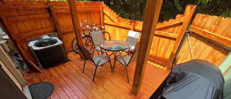 A wooden deck with a barbecue grill, a table with chairs, and a bicycle.