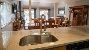 A kitchen with a stainless steel sink, wooden chairs, a dining table, and a cabinet with glass doors. -  Cozy and Dog friendly retreat by Relaxing Creek & Hot tub by Lake Cushman (Hoodsport)