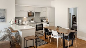 Een moderne keuken met witte kasten, een centraal eiland en een eethoek met een houten tafel en stoelen.