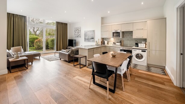 Een moderne woonkamer met een eethoek, keuken en grote ramen.