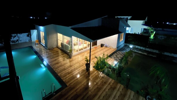 A modern house with a swimming pool, wooden deck, and a patio area with a table and chairs.