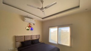 A bedroom with a bed, a ceiling fan, an air conditioner, and a window.