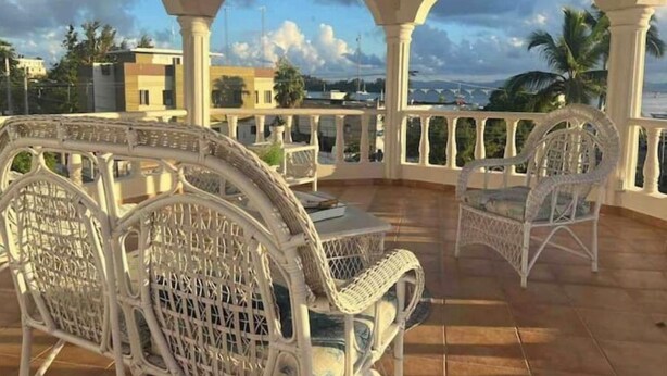 Un patio techado con mobiliario de ratán blanco y vista a la ciudad.