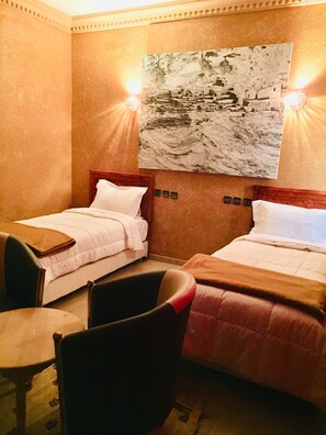 A hotel room with two single beds, a wooden headboard, a small table, and a chair.