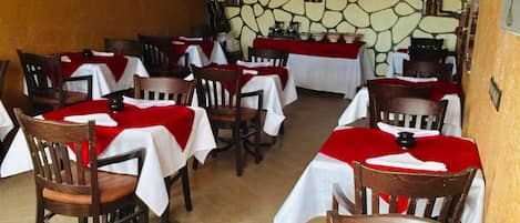 Un ristorante con diversi tavoli ricoperti da tovaglie rosse, sedie di legno e una parete in pietra con un televisore.