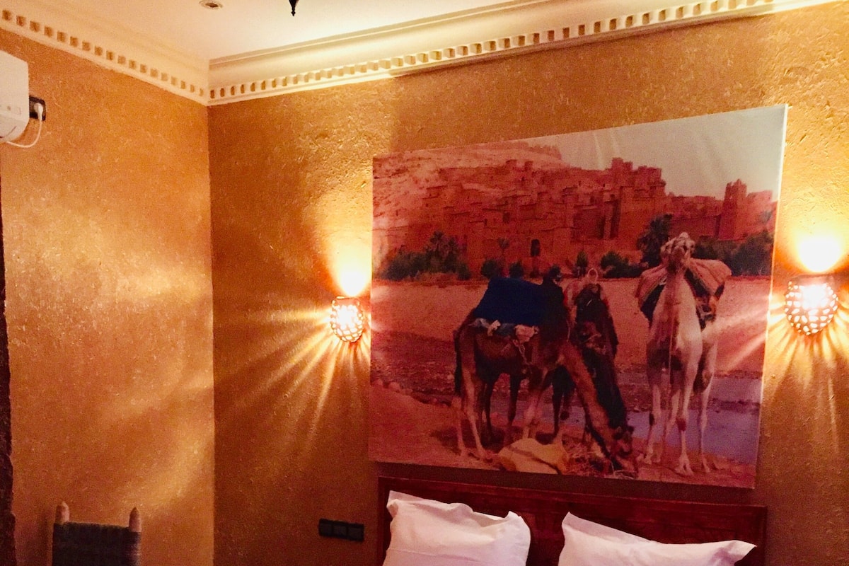 Quarto de hotel com cama, cabeceira, mesa de cabeceira e um quadro na parede.