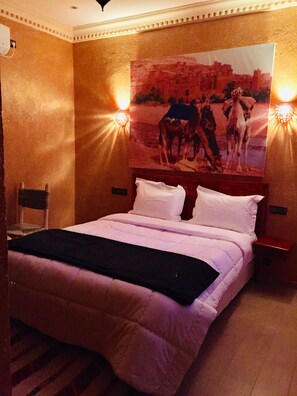 A hotel room with a bed, a headboard, a nightstand, and a wall-mounted picture.