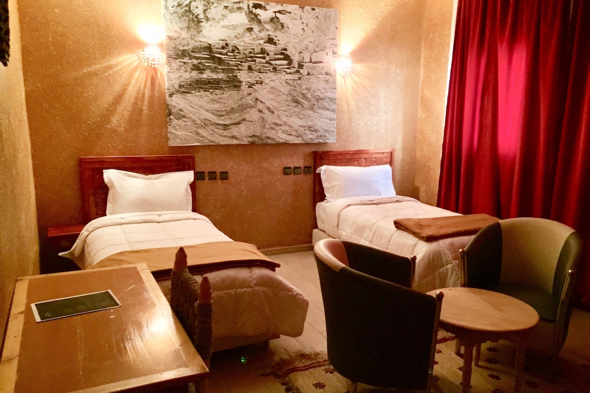 Quarto de hotel com duas camas, uma mesa de madeira, uma cadeira e um quadro na parede.