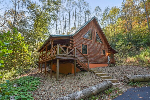A log cabin with a wooden deck and stairs leading to the entrance. - Creekside Serenity | Hocking Hills, Creek, Hot Tub (Logan)
