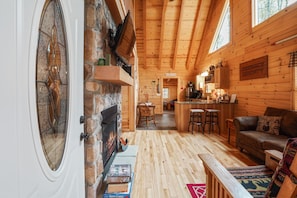 A cozy cabin interior with a stone fireplace, wooden walls, a dining area, and a kitchenette. - Creekside Serenity | Hocking Hills, Creek, Hot Tub (Logan)