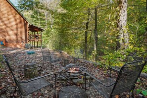 A wooden cabin with a fire pit and metal chairs in a forest setting. - Creekside Serenity | Hocking Hills, Creek, Hot Tub (Logan)