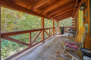 A wooden deck with a view of a forest, a rocking chair, and a table with chairs.