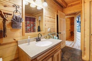 A wooden cabin bathroom with a granite countertop sink, a mirror, and a towel hanging on a hook. - Creekside Serenity | Hocking Hills, Creek, Hot Tub (Logan)
