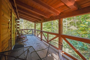 A wooden cabin with a porch, outdoor seating, and a view of a forest.