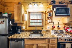 A kitchen with wooden cabinets, a granite countertop, a sink, a stove, and a microwave. - Creekside Serenity | Hocking Hills, Creek, Hot Tub (Logan)