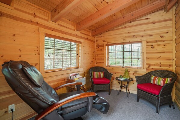 A wooden cabin interior with two wicker chairs with red cushions, a leather recliner, and a small table with a statue. - Creekside Serenity | Hocking Hills, Creek, Hot Tub (Logan)