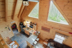 A cabin with a kitchen, dining area, and a large window overlooking a forest.