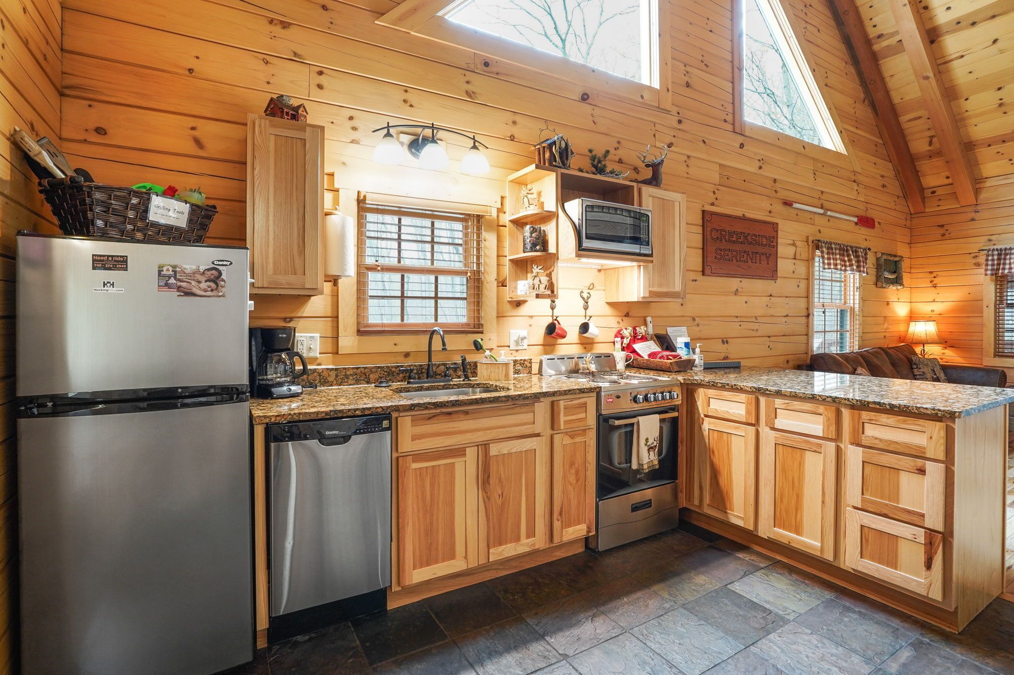 Una cocina estilo cabaña de madera con refrigerador, lavavajillas, estufa y encimeras de granito.