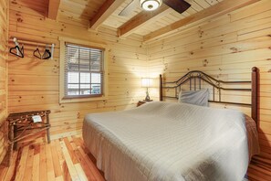 A wooden cabin bedroom with a bed, a nightstand, a lamp, and a window with blinds. - Creekside Serenity | Hocking Hills, Creek, Hot Tub (Logan)