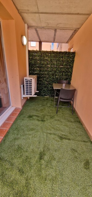 Un petit espace intérieur avec un revêtement de sol en gazon synthétique, une table avec des chaises, un appareil de climatisation et un mur végétal.
