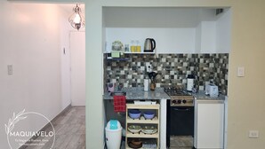 A compact kitchen with a tiled backsplash, a gas stove, a dishwasher, and a small refrigerator. - Amplio y Confortable Monoambiente en el Centro de la Ciudad. A (Buenos Aires)