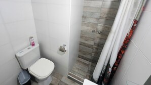 A bathroom with a toilet, a shower with a wooden floor, and a curtain. - Amplio y Confortable Monoambiente en el Centro de la Ciudad. A (Buenos Aires)