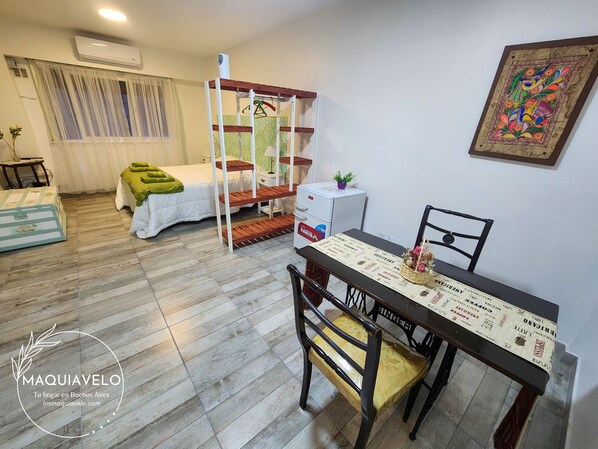 A room with a bunk bed, a dining table with chairs, a small white cabinet, and a colorful wall decoration.