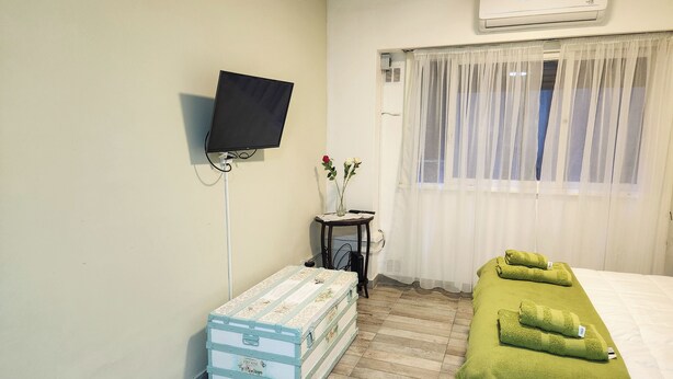 A hotel room with a bed, a small table with a vase of flowers, a television mounted on the wall, and a suitcase on the floor. - Amplio y Confortable Monoambiente en el Centro de la Ciudad. A (Buenos Aires)