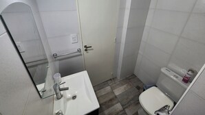 A small bathroom with a white sink, a mirror, a toilet, and a door. - Amplio y Confortable Monoambiente en el Centro de la Ciudad. A (Buenos Aires)