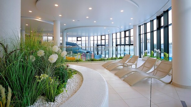 Un espace intérieur moderne doté d’un plafond incurvé, d’un coin salon avec des fauteuils et d’une vue sur un toboggan aquatique.
