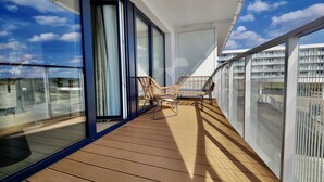 Un balcon doté d’un plancher en bois, de deux fauteuils en osier et d’une porte vitrée.