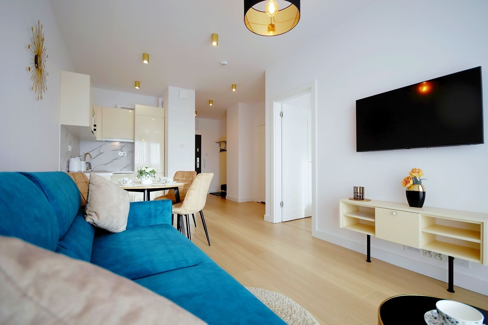 A modern living room with a blue sofa, a flat-screen TV mounted on the wall, and a minimalist design.
