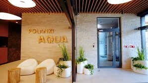 Un espace d’accueil doté d’un plafond en bois, d’une enseigne indiquant « POLANKI AQUA » et de plusieurs jardinières blanches contenant des plantes vertes.