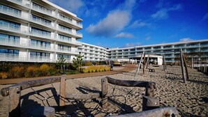Un hôtel moderne doté de nombreux balcons, d’une plage de sable et offrant une vue sur un ciel bleu azur.