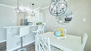 Une cuisine moderne avec des meubles blancs, un îlot central doté de tabourets et des luminaires suspendus.
