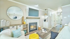 Un salon avec une cheminée, un miroir rond et un canapé agrémenté de coussins décoratifs.