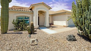 A house with a tiled roof, a central archway, and cacti in the yard. - Pool Home Near Downtown Gilbert! (Gilbert)