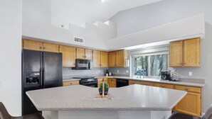 A modern kitchen with a central island, wooden cabinets, a black refrigerator, and a window providing natural light. - Pool Home Near Downtown Gilbert! (Gilbert)
