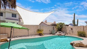 A swimming pool with a curved edge, surrounded by a stone wall, a white canopy, and a green umbrella. - Pool Home Near Downtown Gilbert! (Gilbert)
