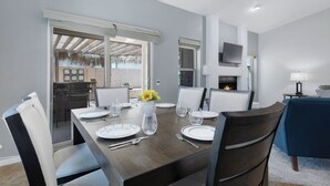 A dining area with a large table set for four, chairs, a vase with flowers, and a television mounted on the wall. - Pool Home Near Downtown Gilbert! (Gilbert)