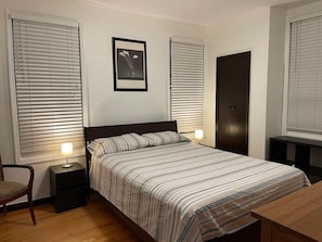 A bedroom with a bed, two bedside tables, a chair, and a door.