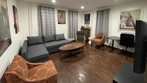 Un salon comprenant un canapé, une table basse, des fauteuils, un téléviseur et un radiateur.